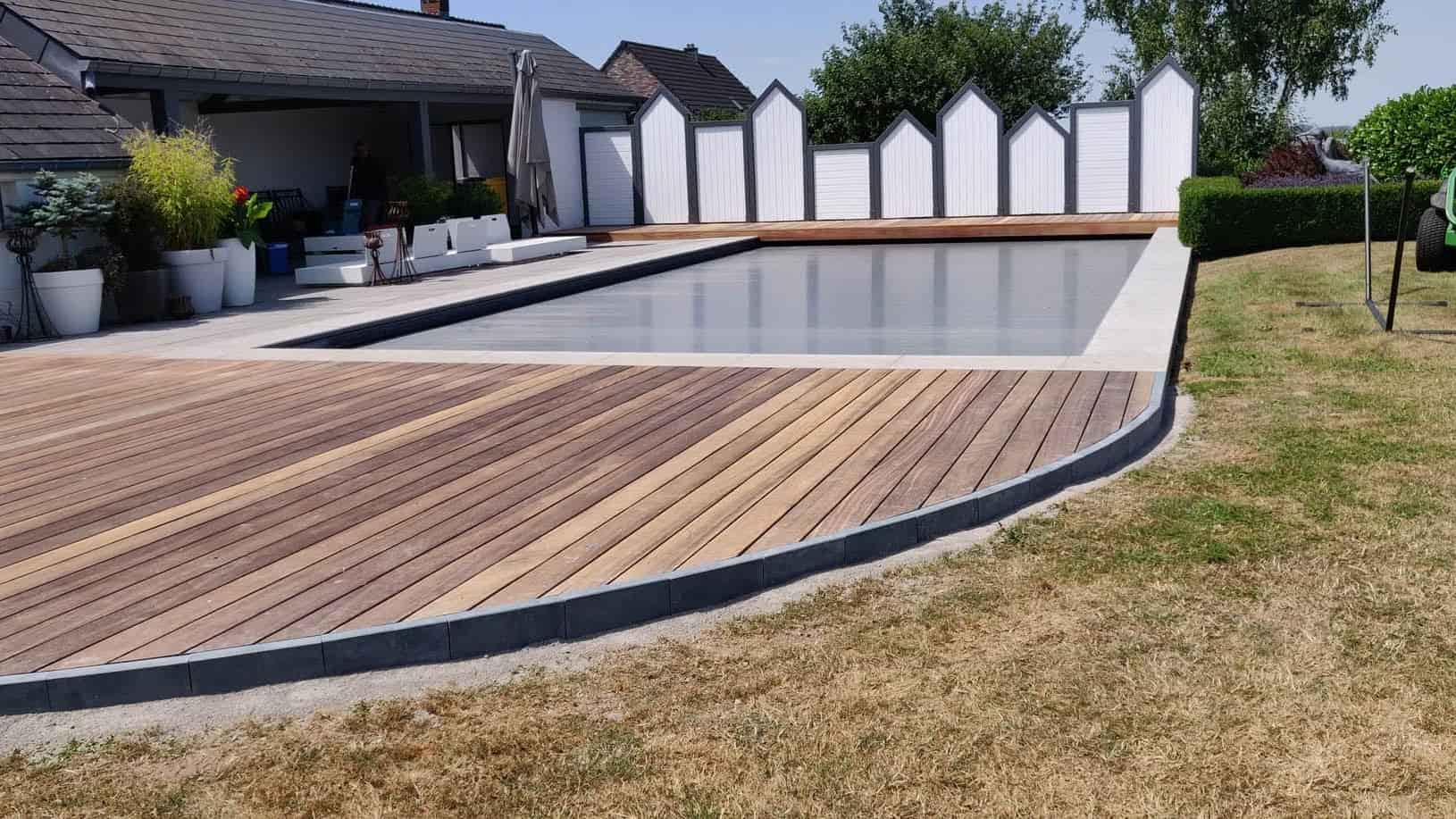 Terrasse en bois exotique posée en courbe autour d'une piscine, bordure en pierre bleue et margelles claires