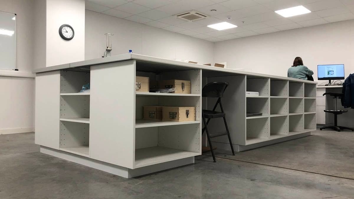 Agencement sur mesure en îlot dans un local professionnel : caissons ouverts, casiers et plan de travail continu