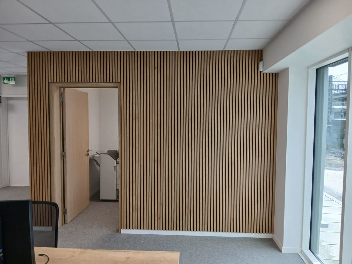 Salle de bureau terminée : mur en tasseaux de bois, bloc-porte et son encadrement, faux plafond à dalles et éclairage encastré