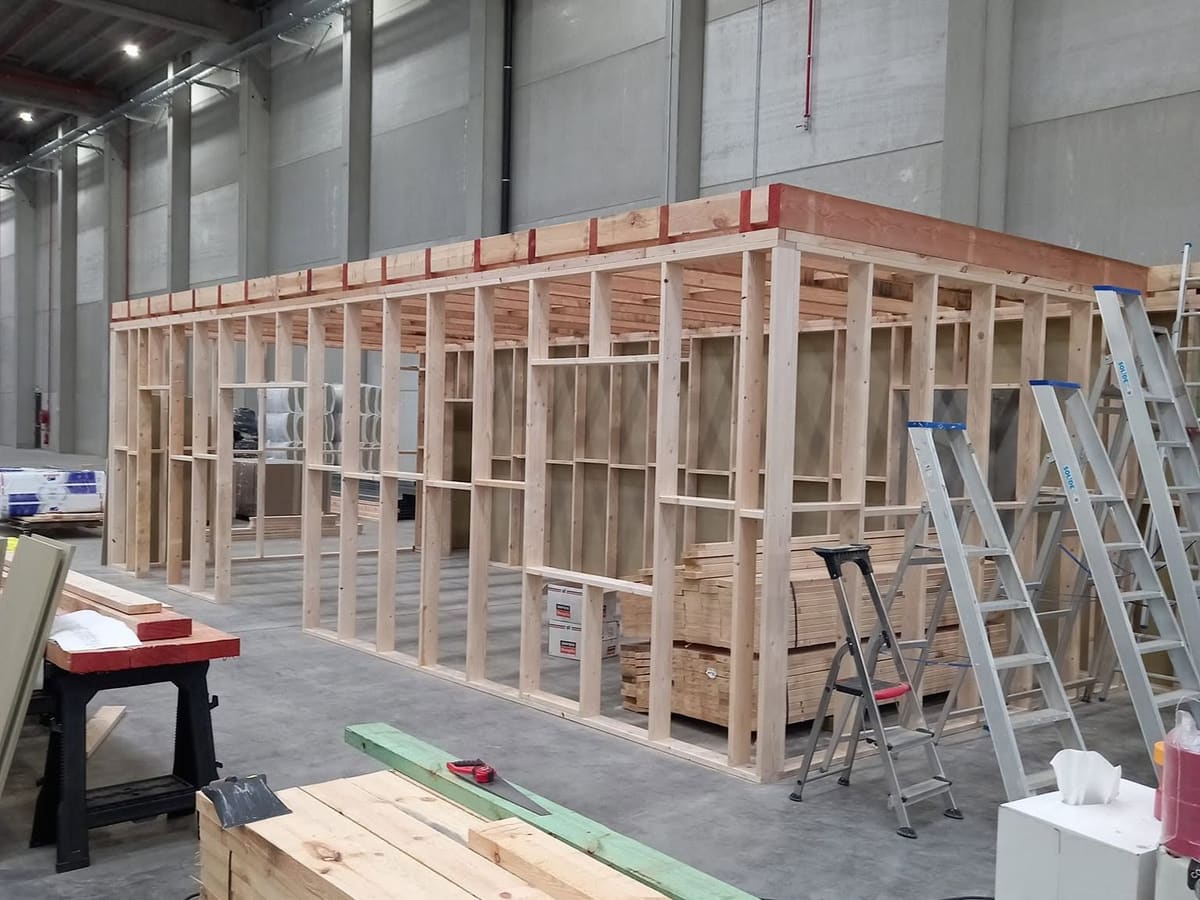 Ossature bois montée dans un hall industriel : montants, traverses et linteaux assemblés, bois de charpente stocké au premier plan