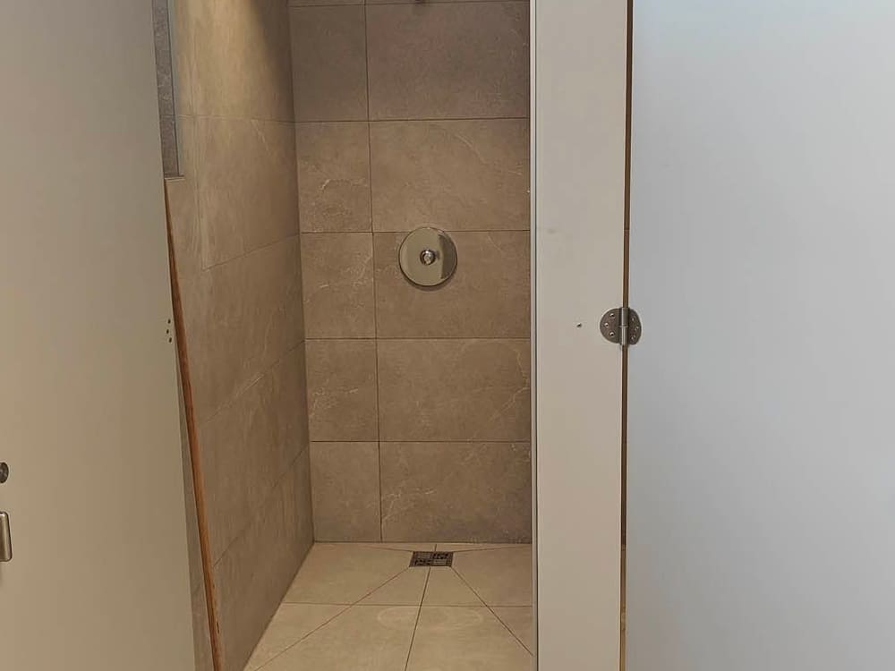 Cabine de douche collective carrelée, avec évacuation de sol encastrée, vue depuis le passage entre deux cloisons de cabines