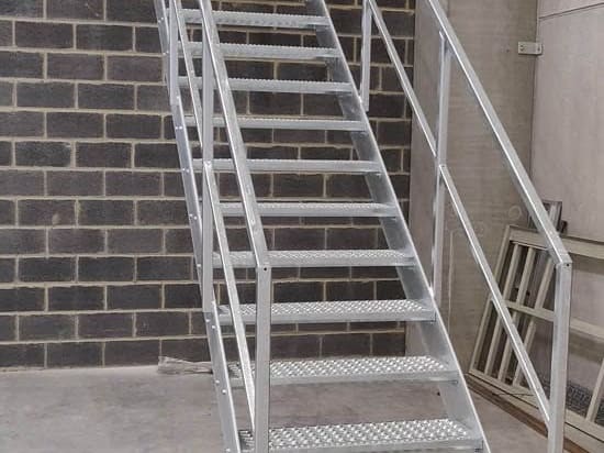 Escalier droit en acier galvanisé posé dans un hall, marches en tôle larmée et garde-corps à lisses