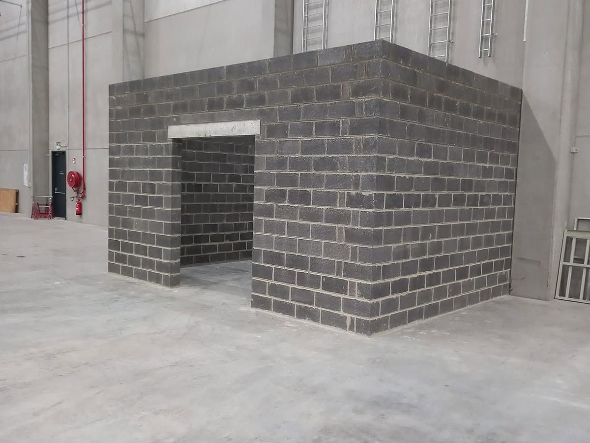 Local maçonné en blocs de béton monté à l'intérieur d'un hall, avec linteau posé au-dessus de l'ouverture de passage