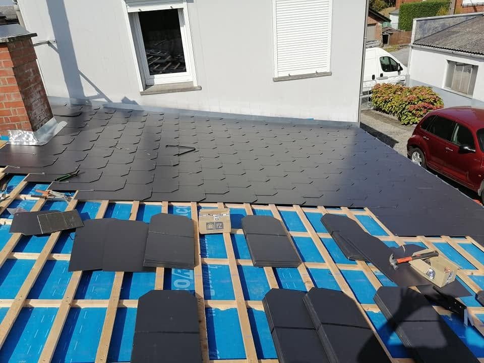 Pose d'ardoises en cours : liteaunage sur écran de sous-toiture bleu, rangs déjà posés en partie haute et ardoises en attente
