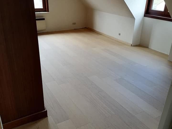 Pièce aménagée sous rampants avec parquet clair posé et joues de lucarnes plafonnées et peintes en blanc