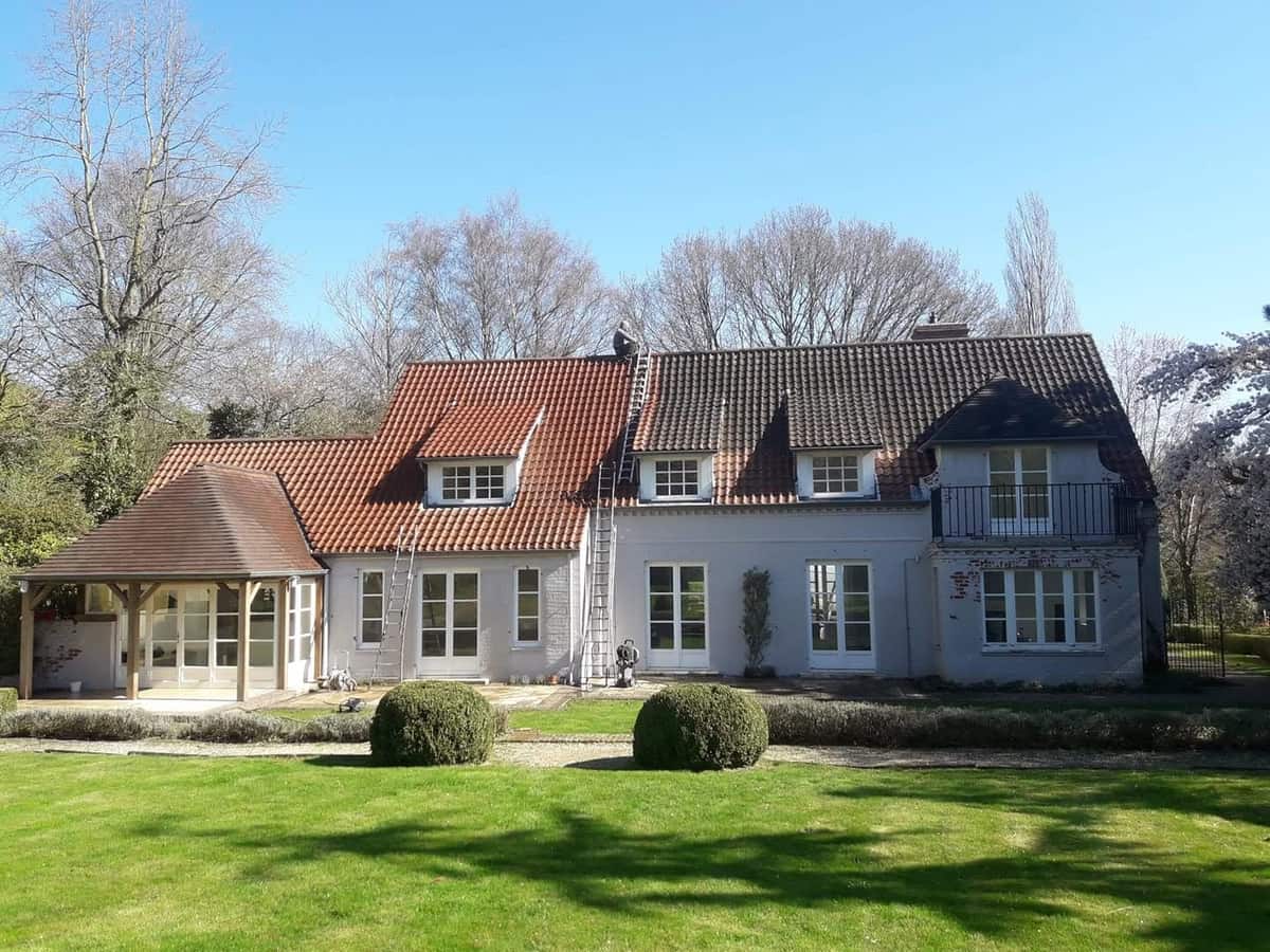 Façade arrière d'une maison remise en peinture, avec une toiture en tuiles démoussée sur la moitié gauche du versant