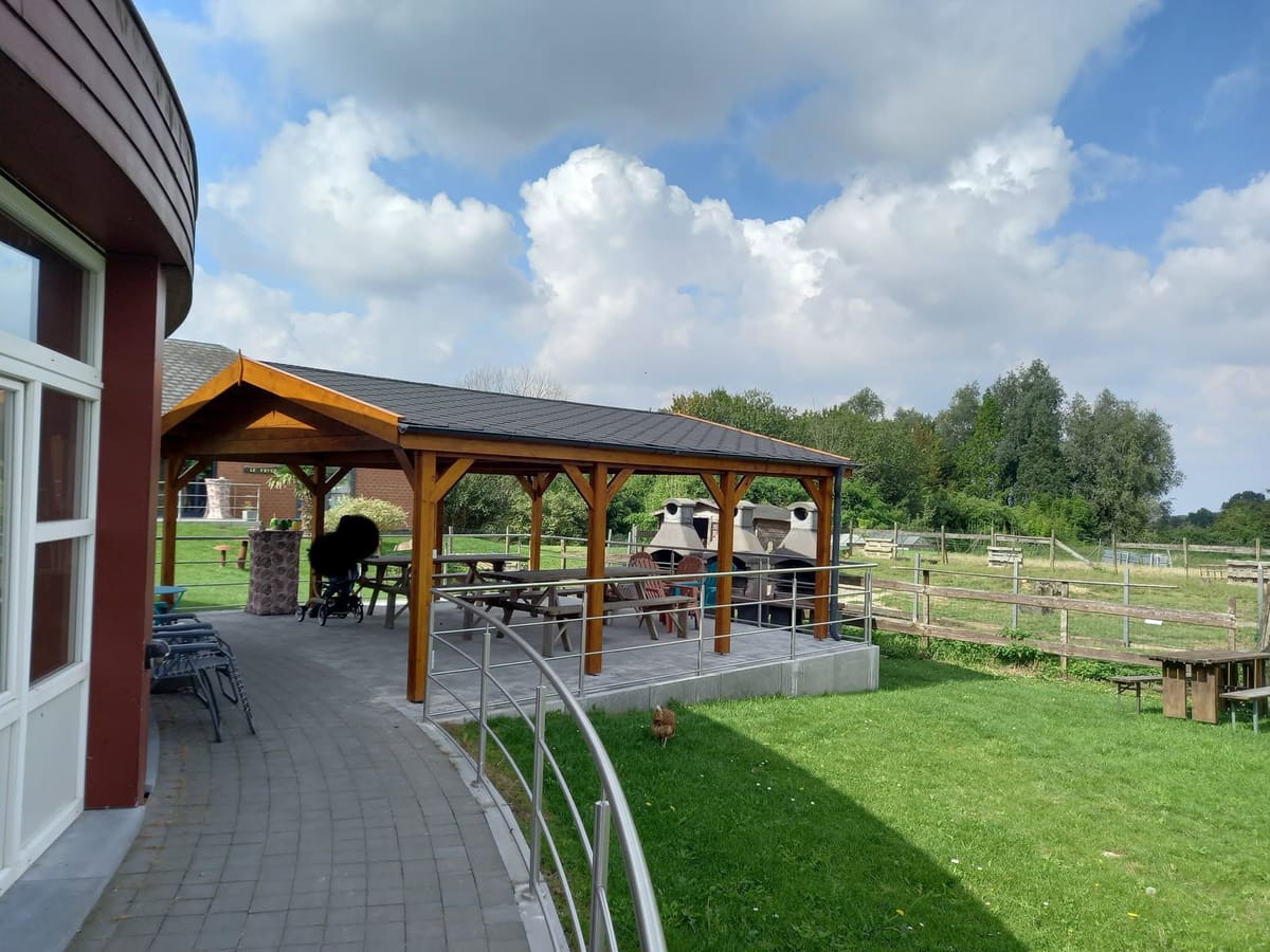 Pergola en bois couverte, montée sur une terrasse extérieure et bordée d'un garde-corps métallique