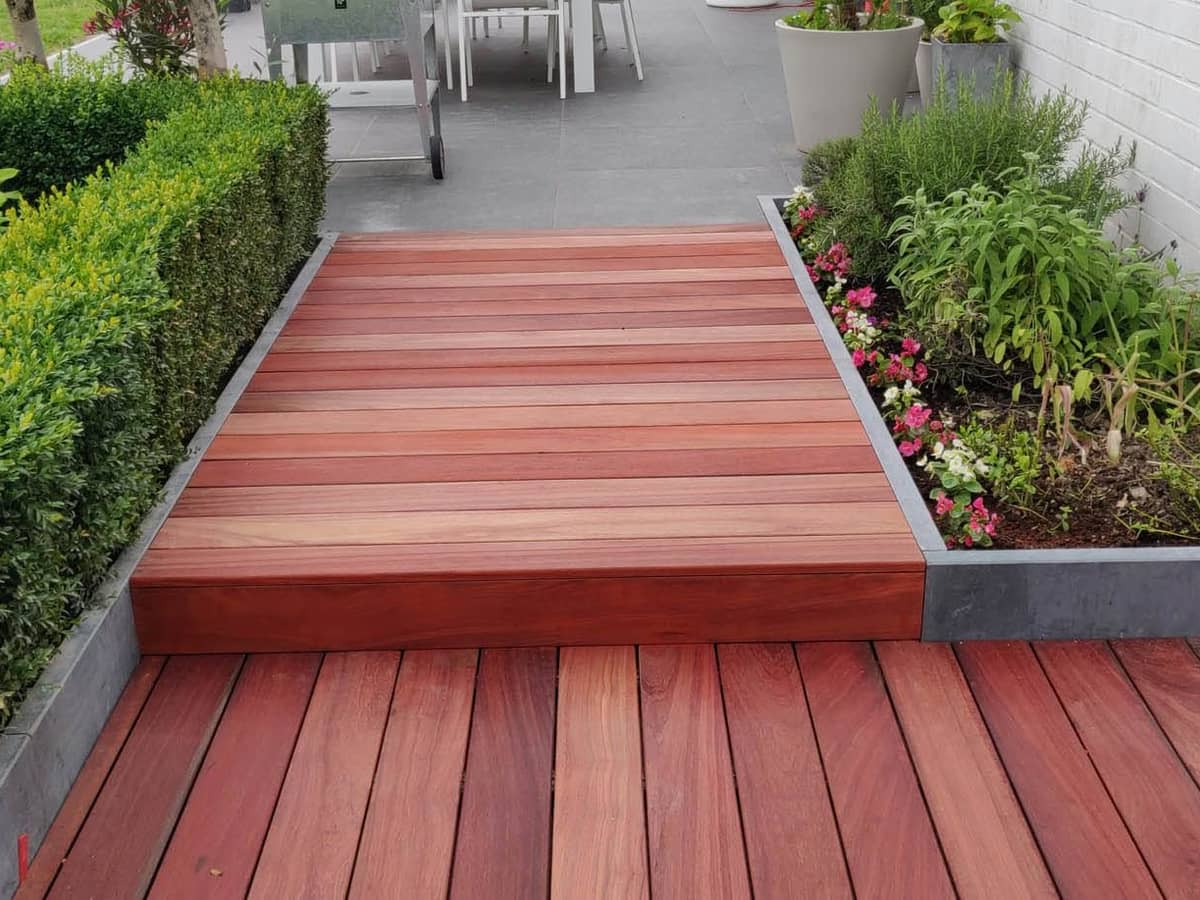 Terrasse en bois exotique sur deux niveaux reliés par un emmarchement, bordures en pierre bleue et massifs plantés