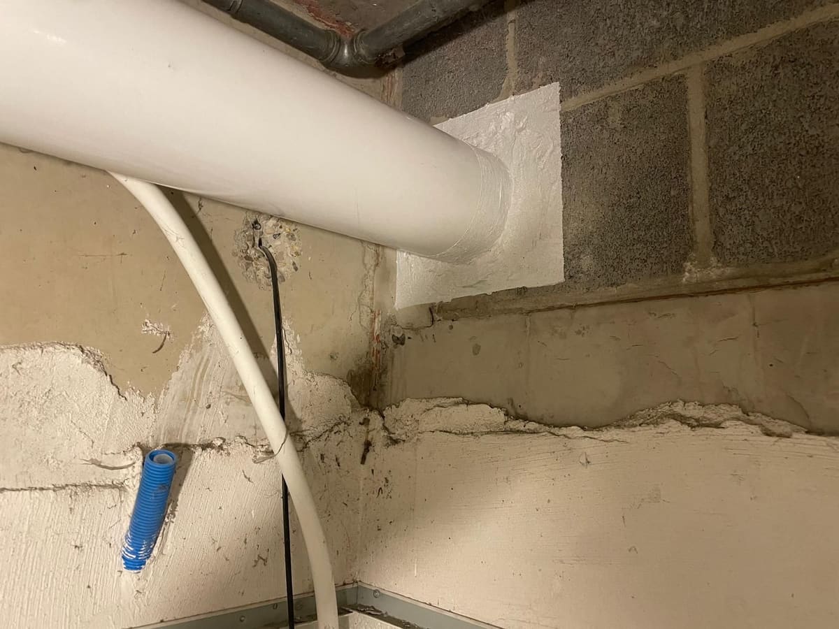 Traversées de cloison calfeutrées : le passage d'une descente et d'un câble à travers un mur en blocs a été rebouché et enduit