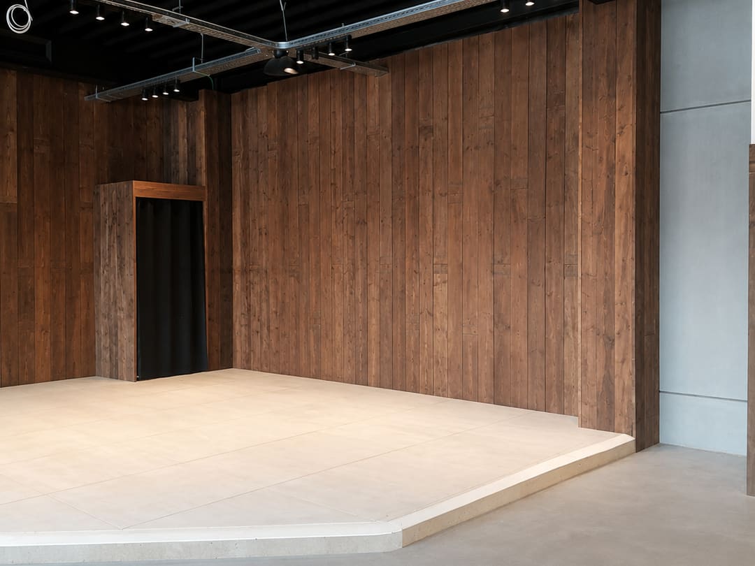 Bardage intérieur en lames de bois posé toute hauteur dans un espace commercial, avec podium et rail d'éclairage