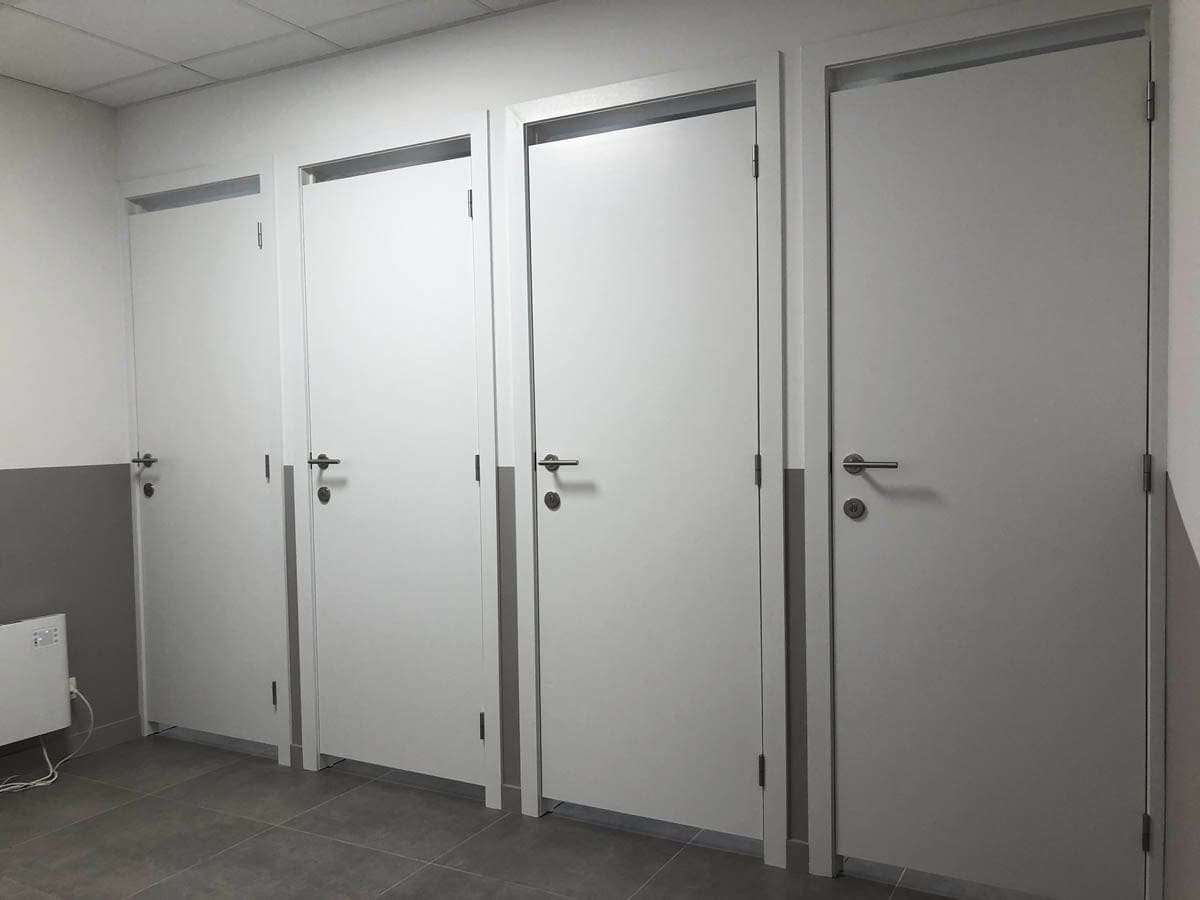 Quatre blocs-portes alignés dans un local sanitaire, huisseries peintes, quincaillerie et condamnations posées