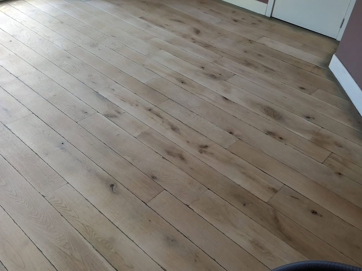 Parquet en chêne à larges lames après ponçage, prêt à recevoir sa finition, plinthes blanches en périphérie