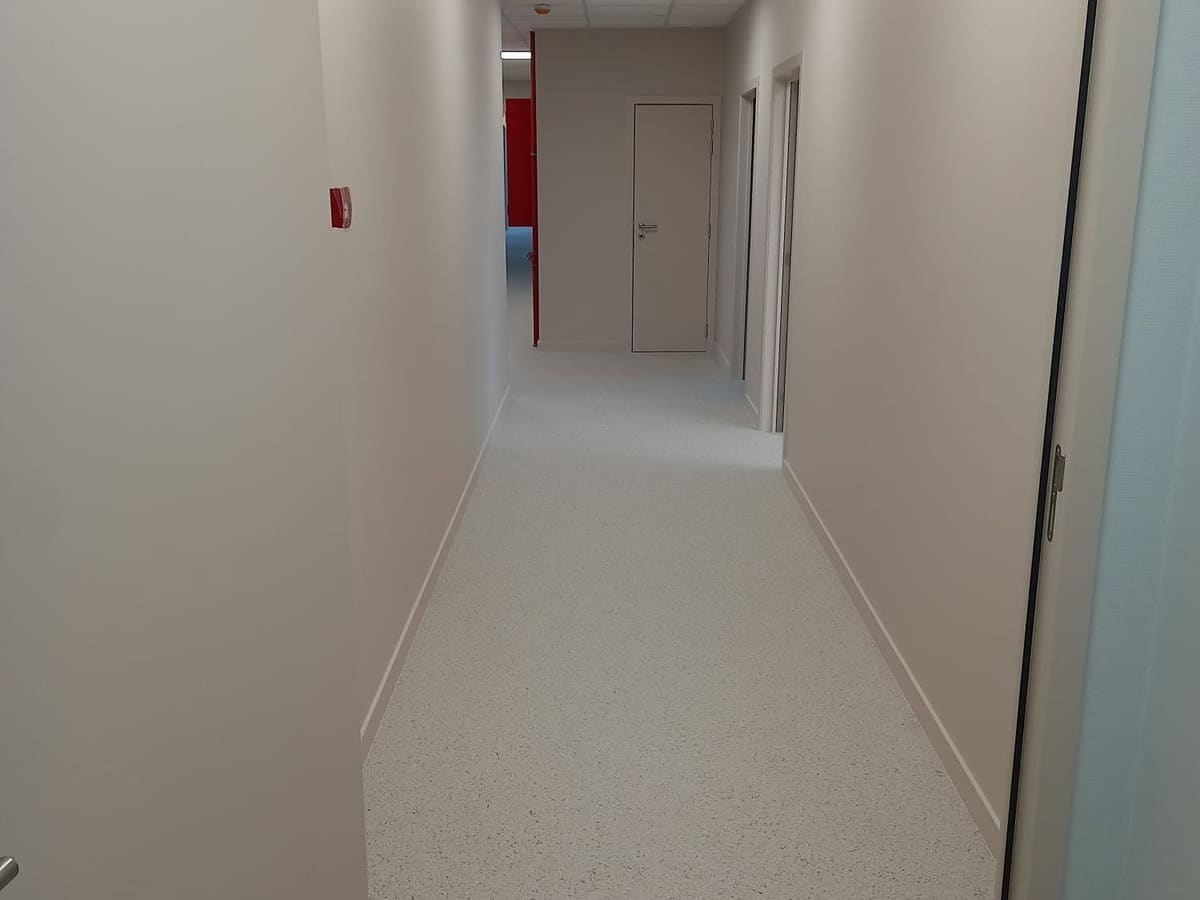 Couloir livré avec un sol souple clair posé en lés et remonté en plinthe, faux plafond éclairé et blocs-portes peints