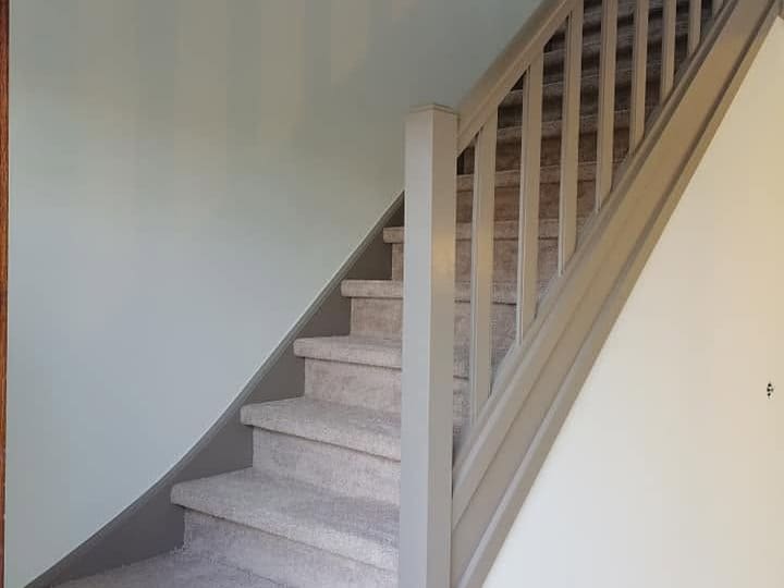 Cage d'escalier repeinte : mur d'accent vert d'eau, rampe et balustres laqués, marches habillées de moquette