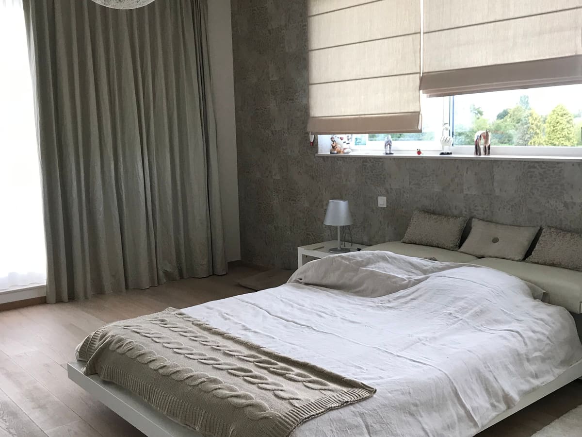 Chambre terminée avec un revêtement mural texturé en tête de lit, parquet clair et rideaux toute hauteur