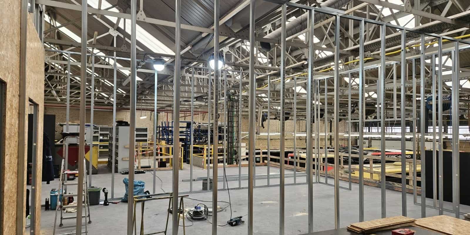Ossatures métalliques et panneaux de cloisons montés dans un hall industriel, en cours de chantier