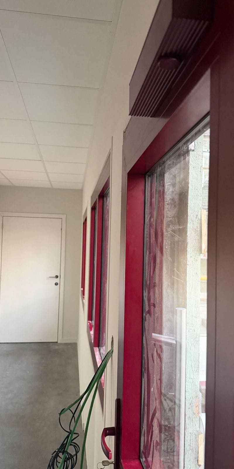 Couloir terminé dans un hall industriel — cloisons peintes, faux plafond acoustique, porte posée et bardage rouge