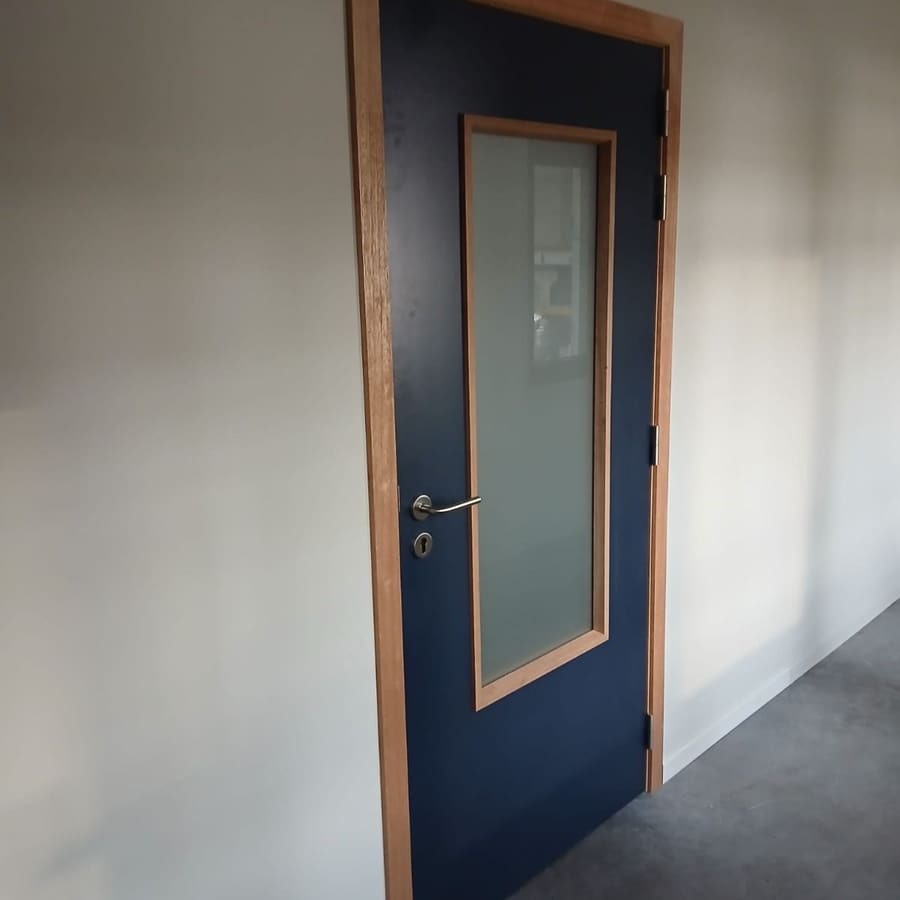 Porte vitrée bleue et son encadrement bois posés dans une cloison neuve peinte