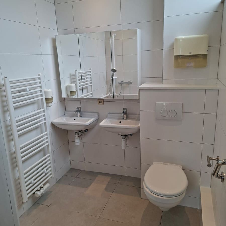 Salle de bain adaptée — WC suspendu avec barres d’appui, lavabo, sèche-serviettes et carrelage posé du sol au plafond